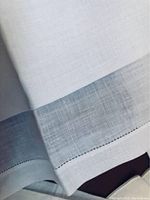 Close-up of fine linen fabric with detailed hemstitching and subtle white woven pattern