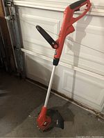 Full view of the electric trimmer/edger showing orange handle, metallic shaft, and black guard.