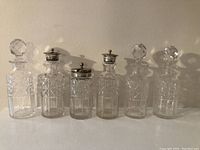 Front view of six cut glass cruet bottles and condiment holder, showing faceted glass design and silver plated tops.