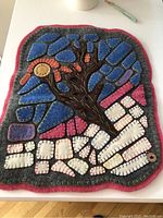 Overall view of colorful felt wall hanging with tree and abstract shapes on a flat surface