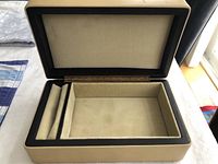 Open view of vintage jewelry box interior showing beige velvet lining and padded sections for rings or cuff links