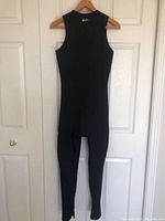 Front view of the full-length black sleeveless wetsuit hanging on a wooden hanger against a white door.
