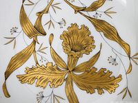 Close-up of intricate gold leaf floral decoration with black line detail on white porcelain surface