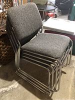 Four stackable dining chairs upholstered in grey tweedy fabric with tubular chrome frames stacked together.