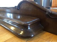 Close-up of carved decorative edge and shelf detail showing polished walnut wood and scroll carving.