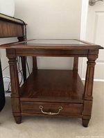 Front view of solid wood side table with glass top, showing square carved legs and bottom shelf.