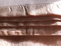 Close-up photo of the blanket's satin trim edge in pale dusty rose color.
