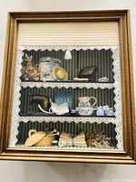 Frontal view showing all three shelves inside the wooden shadow box, with vintage and handmade miniature sewing and knitting items arranged neatly, including miniature Singer sewing machine, mirror, hat box, ceramic jug and bowl, dried flowers, knitting basket with wool, and linen bundle.