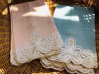 Two folded fingertip towels, one soft pink and one blue, showing monogram D.N.P. and decorative open lacework on edge.