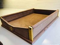 Side view of suede leather document tray showing brass corner accents and front buckle in warm taupe color.