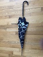 Full view of the closed umbrella showing black and white geometric patterned canopy and black curved handle.