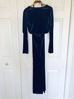 Full-length image of the dark teal velvet gown and matching bolero jacket hung on a door, showing fabric texture and color.