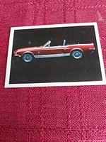 Front of collectible card showing a red 1968 Mustang Shelby convertible with white side stripe, black background, and white border.