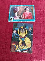 Photo showing two novelty collectors cards: one from the movie E.T. depicting E.T. and a child with caption 'Sighting the Aliens', and the other a Marvel Comics card featuring X-Men character Wolverine in classic costume.