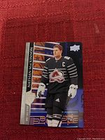 Close-up of Nathan MacKinnon hockey card showing player in black Colorado Avalanche All-Star jersey with Upper Deck logo and name visible.