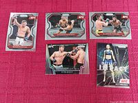 Photo showing 5 Prizm UFC cards laid out on a red cloth: Brandon Royval Rookie, Deiveson Figueiredo, Aljamain Sterling, Stipe Miocic Knockout Artists, Rose Namajunas Instant Impact.
