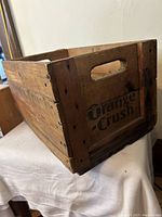 Side view of Orange Crush branded wooden crate showing the logo, wood grain, and nailed construction.