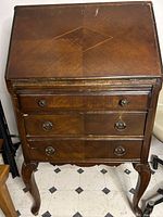 Full front view of the antique wooden secretary desk showing the fold-over top and three drawers with metal handles.