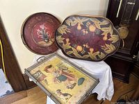 Three antique metal serving trays stacked, showing various decorative motifs and styles