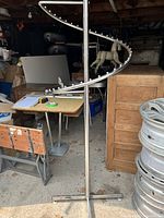 Full view of the metal spiral clothing display rack with cross base inside a storage space showing its height and shape.