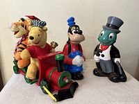Full lot displaying all three items: Pooh and Tigger plush toy train engine, Goofy figurine, and Jiminy Cricket figurine.