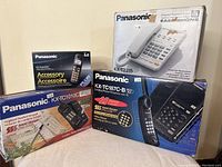 Four Panasonic landline telephones and accessory box displayed with packaging, showing product branding and details