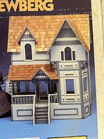 Closed original box showing the Newberg miniature doll house with Tudor-style design, shingled roof, and detailed front porch.