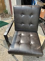 Close-up of brown leather office chair showing button tuft details, metal armrests, modern cantilever frame and visible wear marks