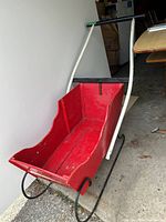 Full view of the red wooden sleigh with white handles inside a garage-like space.