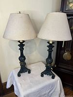 Pair of dark green table lamps with ornate bases and cream fabric shades on a table.