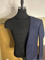 Front view of black fabric male torso mannequin with navy jacket draped over one shoulder.