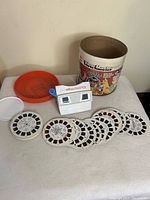View-Master viewer, cylindrical container, and several View-Master disks displayed flat