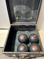 Open black carrying case showing four black bocce balls with red number markings inside.