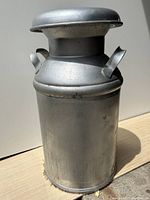 Front and side view of the silver vintage metal milk can showing handles and body shape