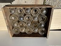 Top view showing 20 glass insulators arranged in wooden box, visible variations in shape on top edges.