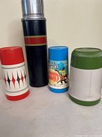 Four vintage thermoses arranged side by side showing various colors and designs.
