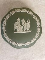 Top view of green Wedgwood jasperware container lid with white classical relief figures and laurel wreath border