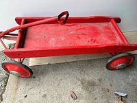 Full side angle view of the red wooden wagon with metal handle and wheels.