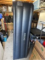 Full view of black Intex air mattress standing upright showing brand name and horizontal air chambers.