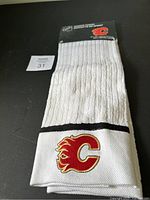 Full view of folded white sports towel with Calgary Flames logo embroidered on the front edge, laying on a black surface with lot number card.