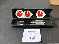 Three Calgary Flames branded darts neatly arranged in a black plastic case. Flights show the red Flames logo on a white background. Metal barrels and black stems are visible.