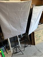 Two white diffusion softboxes fully set up on black adjustable tripod stands in a garage or storage space.