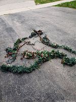 Full length of the laid-out Christmas garland on pavement, showing overall size and shape with visible green pine needles and integrated string lights.