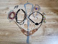 Collection of assorted costume jewelry displayed on wooden surface including various necklaces and a pair of earrings.