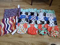 Set of 20 colorful cloth diaper shells arranged in rows with two fabric wet bags on the side. Various patterns with multiple snap buttons on each diaper shell.