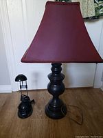 Large black table lamp with red shade and small black desk lamp shown side by side on floor