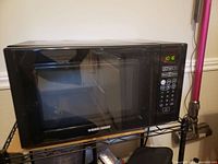 Front angled view of black Black+Decker microwave showing door and digital control panel illuminated.