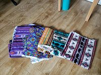 Lot of five cotton fabric pieces with various colorful patterns laid flat on wooden floor.