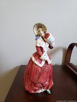 Front side of the Royal Doulton Christmas Morn porcelain figurine showing the detailed facial features, bonnet, white fur-lined cape, and red skirt with a muff in the figure's hands.