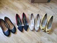 Four pairs of women's high heels (black, red/black/white, gold, yellow) arranged side by side on wood floor showing condition and style.